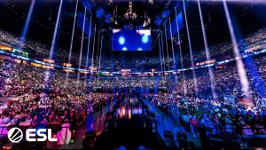 A imagem mostra uma grande arena chamada The Palladium, em Colônia, Alemanha, lotada de público durante um evento da ESL. A iluminação intensa e os efeitos de luz criam um ambiente vibrante, com milhares de fãs assistindo a uma competição emocionante. O palco está preparado para apresentações, com um telão grande visível acima.